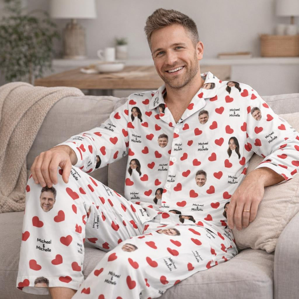 Man wearing a white pajama set with red hearts and printed faces, sitting on a couch.